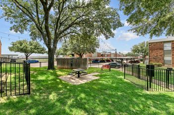 A black fence surrounds a green lawn with a picnic table in the middle.